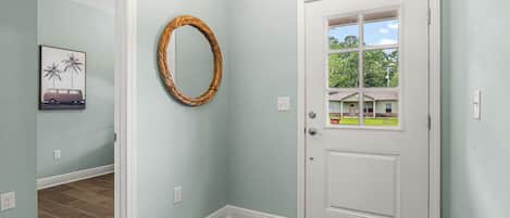 A hallway with a white door, a framed picture, and a woven wall decoration.