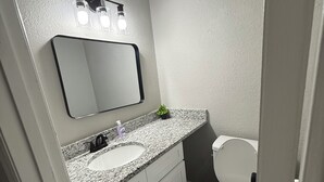 Et badeværelse med en hvid vask, et spejl, et toilet og en lille plante på bordpladen.
