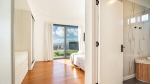 A modern bedroom with a large bed, a sliding glass door to a balcony, and a bathroom with a marble wall.