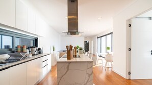 A modern kitchen with white cabinetry, a marble island, and a dining area with white chairs and a table.
