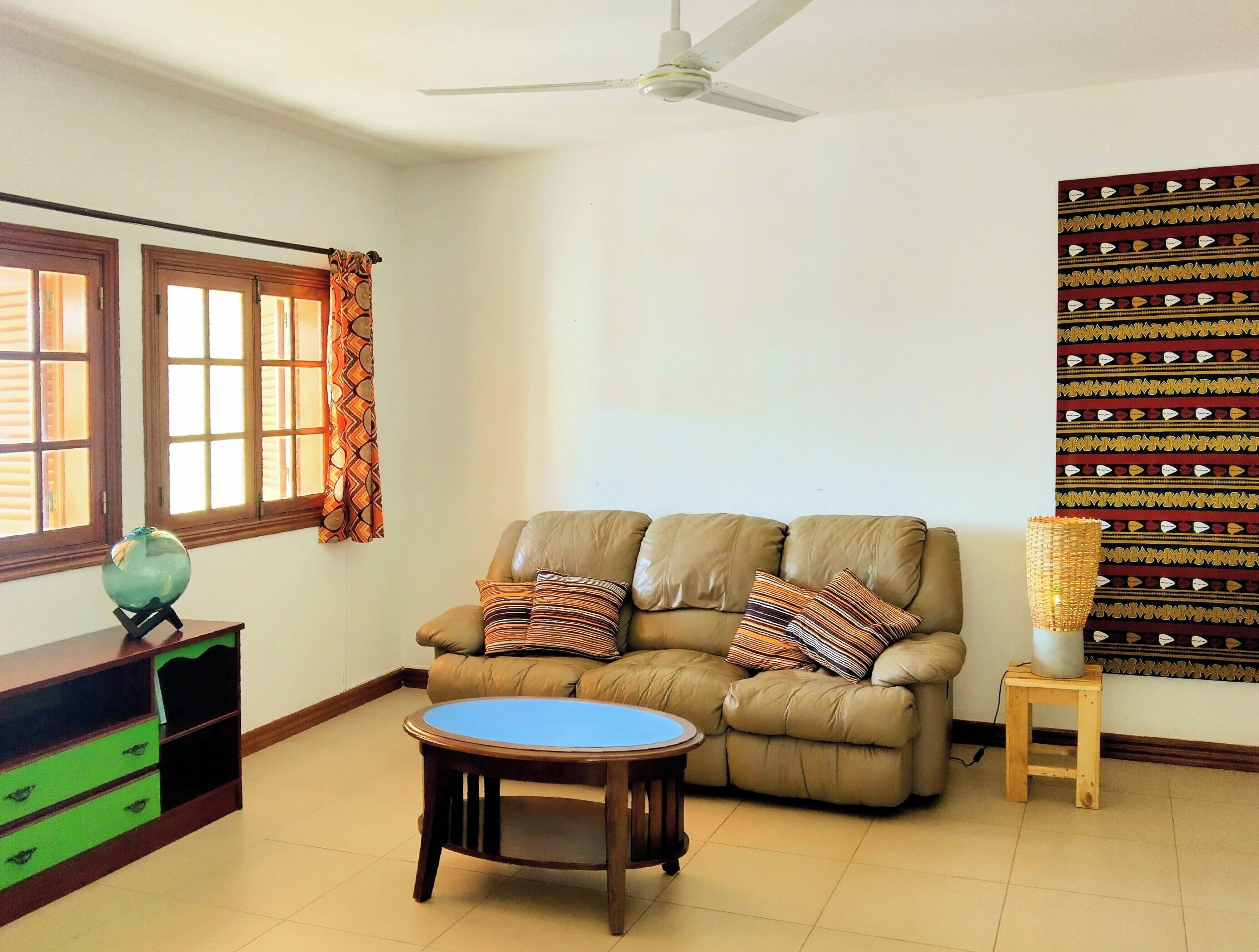 A living room with a sofa, a round coffee table, a small wooden stool, and a patterned wall hanging.