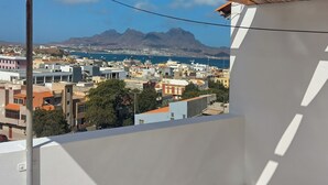 A balcony with a view of a coastal town, buildings, and mountains.