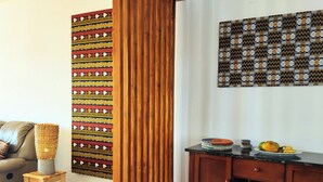 A living room with a sofa, a wooden cabinet, a patterned wall hanging, and a small stool.