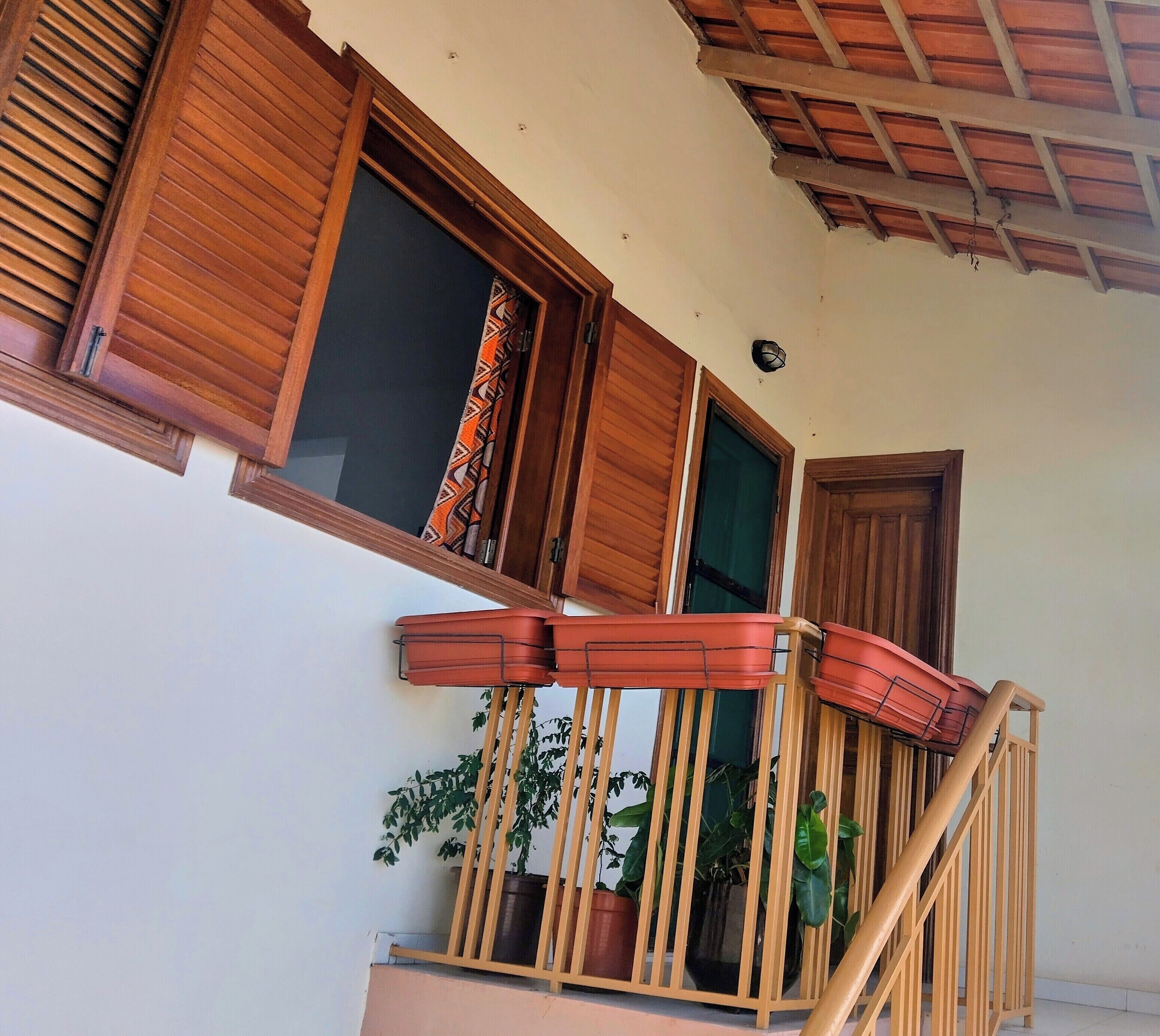 A balcony with wooden railings, potted plants, and a window with wooden shutters.