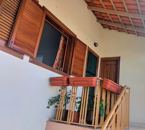 Un balcón con barandilla de madera, plantas en macetas y una ventana con contraventanas de madera.