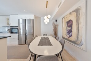 A modern kitchen with stainless steel appliances, a dining area with a round table, and a large abstract painting on the wall. - Holiday Home 'Beautiful 4 bedroom Townhouse' with Shared Pool, Wi-Fi and Air Conditioning (Marbella)