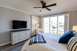 A hotel room with a bed, a television, a ceiling fan, a window with a view, and a white dresser. - Beach Please Condo Beach View (Rosemary Beach)