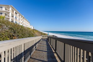 A wooden boardwalk leading to a beachfront hotel with balconies overlooking the ocean. - Beach Please Condo Beach View (Rosemary Beach)