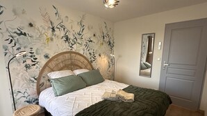 A bedroom with a bed, a woven headboard, a green throw blanket, a mirror, and a door. - Charming cottage with garden and pets allowed in Allier (Buxières-les-Mines)