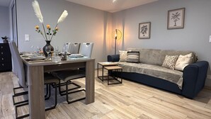 A modern living room with a dining area, featuring a wooden dining table, a sofa, and a floor lamp. - Charming cottage with garden and pets allowed in Allier (Buxières-les-Mines)