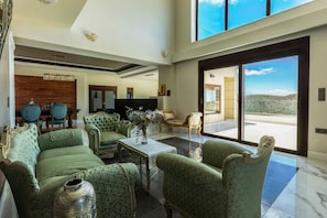 Ein geräumiges Wohnzimmer mit grünen Polstermöbeln, einer Chandelüster und einem großen Fenster mit Blick auf die Landschaft.