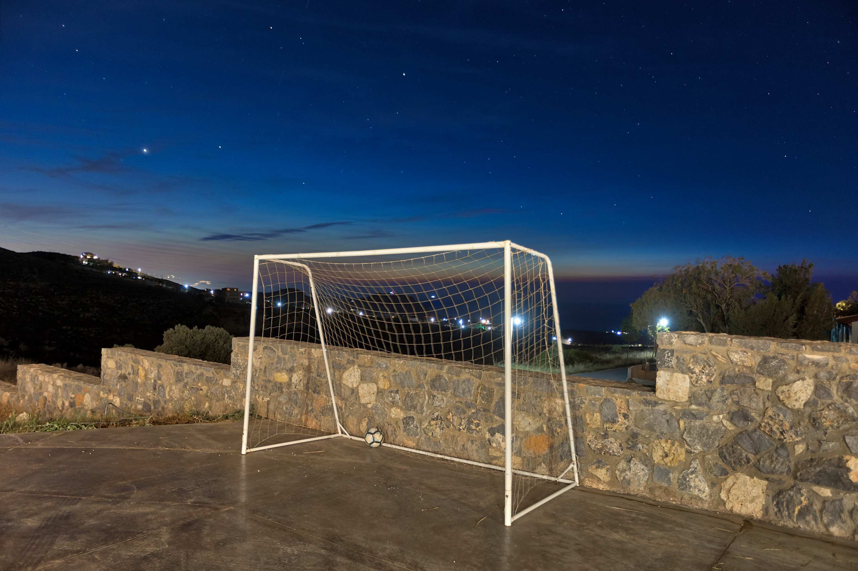 A soccer goal with a net, surrounded by stone walls, under a night sky with stars.