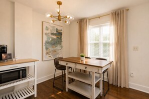 A dining area with a wooden table, chairs, a chandelier, a painting, and a window with curtains. - Historic Uptown 2BD 1BA - 8 min to Downtown & Pier (St. Petersburg)
