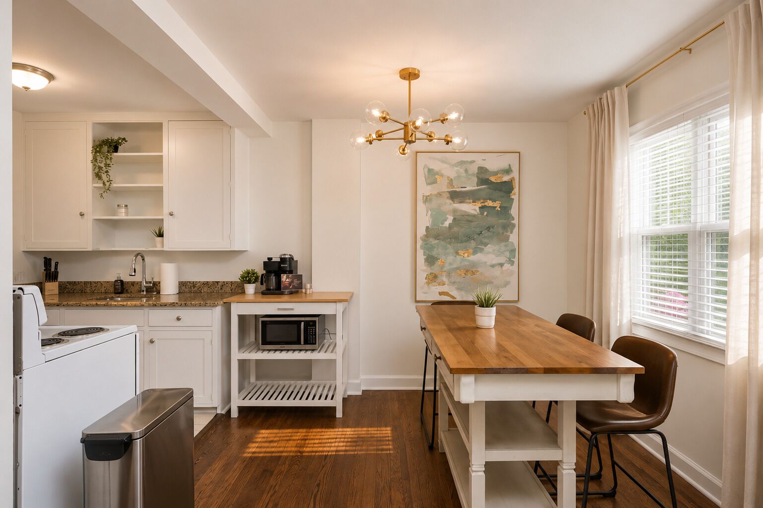 Een moderne keuken met witte kasten, een houten eettafel en een groot raam met jaloezieën.