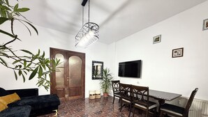 A living room with a dark-colored sofa, a dining table with chairs, a TV mounted on the wall, and a patterned tiled floor. -  Accommodates up to 6 guests,Free parking,Near Amazonia Aquapark,Iulius Town (Timișoara)