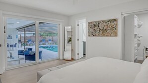 Une chambre dotée d’un grand lit, d’un ventilateur de plafond, d’une porte-fenêtre coulissante donnant sur une zone piscine et d’une œuvre d’art accrochée au mur.