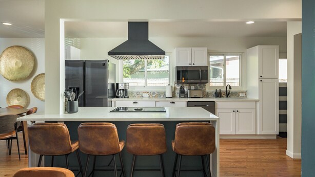 Una cocina moderna con una isla central, armarios blancos, electrodomésticos de acero inoxidable y un amplio ventanal.