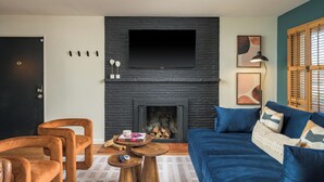 Una sala de estar moderna con chimenea, un televisor de pantalla plana sobre ella, un sofá azul y una mesa de centro de madera.
