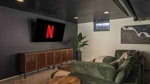 Una sala de estar moderna con un televisor de pantalla plana grande montado en la pared, una mesa consola de madera, un sofá verde y una planta en maceta.