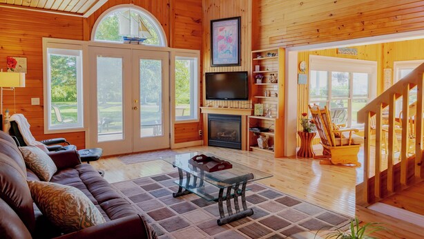 Interior de madera con sofá, una mesa de centro de vidrio, chimenea, televisor y una escalera.