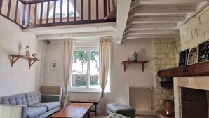 Un salon comprenant un canapé, un pouf, une table en bois, une cheminée et une vue sur l’extérieur par une fenêtre.