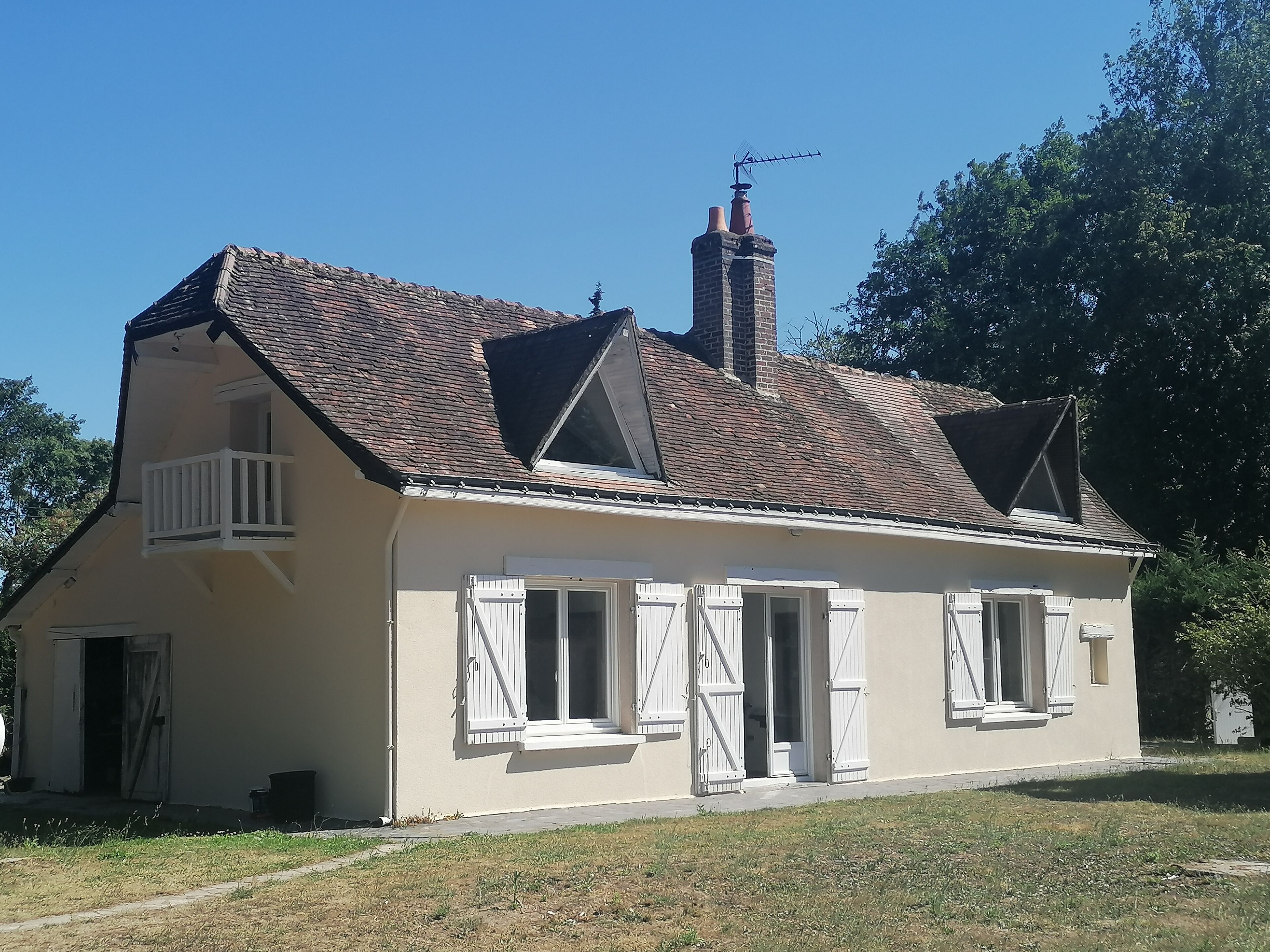 A two-story house with a sloped roof, white shutters, and a small balcony.