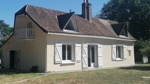 Une maison à deux étages, avec un toit en pente, des volets blancs et un petit balcon.