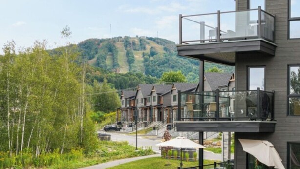 Ein modernes Gebäude mit einem Balkon mit Blick auf eine Wohngegend und eine Hügelkette im Hintergrund.