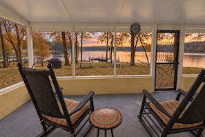 A porch with two rocking chairs facing a lake, a picnic table, and a view of trees and a dock.