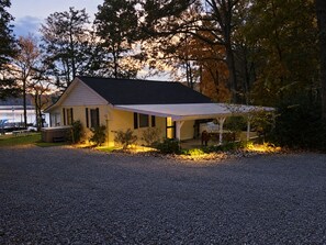 A single-story house with a covered porch, a gravel driveway, and a dock with boats.