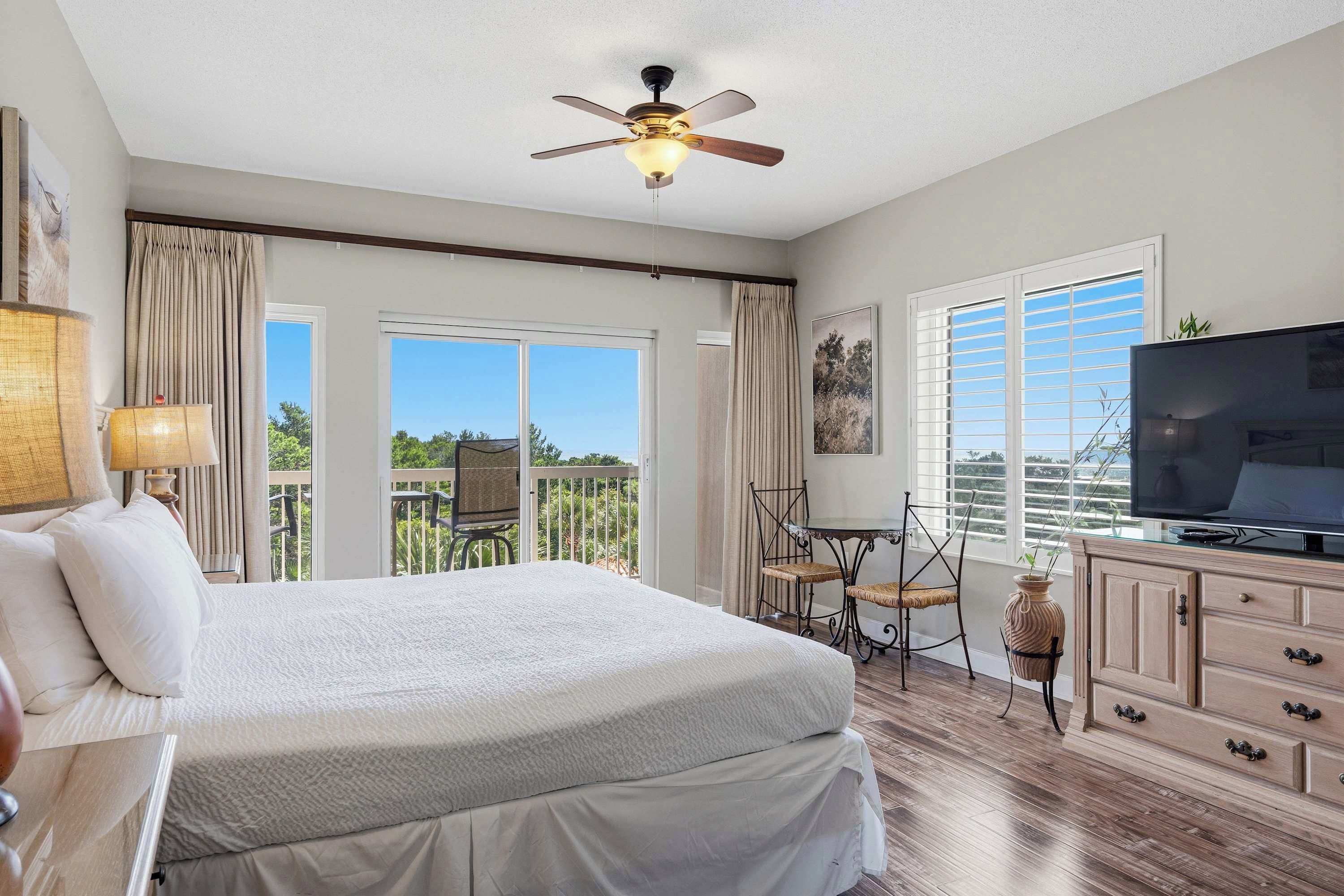 A hotel room with a bed, a television, a dining table with chairs, and a balcony with curtains.
