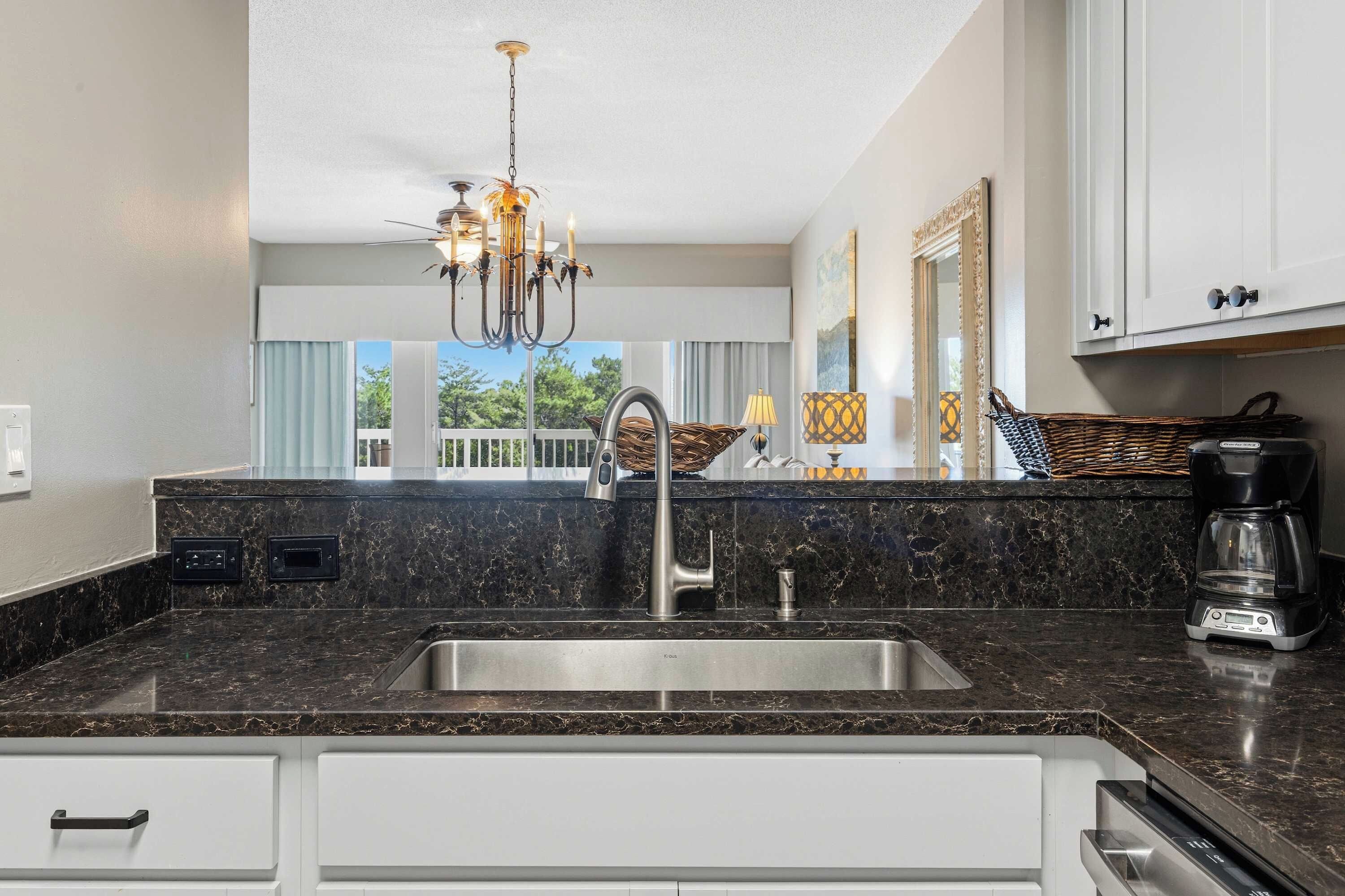 A modern kitchen with a marble countertop, stainless steel sink, and a chandelier.