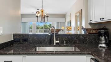 A modern kitchen with a marble countertop, stainless steel sink, and a chandelier.