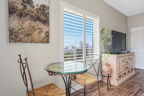 Une pièce avec une table et des chaises en verre, un téléviseur posé sur un meuble et un tableau accroché au mur.