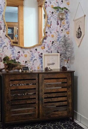 A wooden console table with a mirror, floral wallpaper, and decorative items.