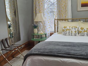 A neatly arranged bedroom with a bed, a bedside table with a lamp, a chair, and a window with curtains.
