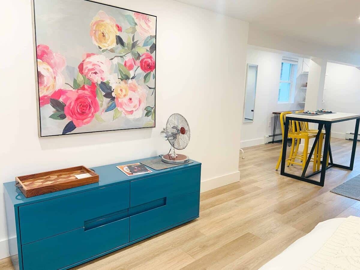 Una sala de estar moderna con un mueble azul turquesa, un ventilador y un cuadro con motivos florales en la pared.