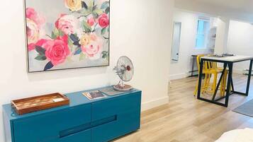 Una sala de estar moderna con un mueble azul turquesa, un ventilador y un cuadro con motivos florales en la pared.