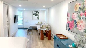A modern bedroom with a bed, a desk, a chair, a sofa, and a wall-mounted TV. - Fresh + Modern Garden Level Kittery Studio (Kittery)