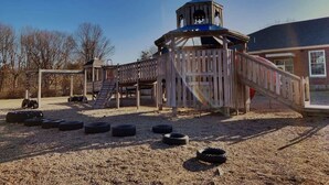 A playground with a wooden structure, a slide, and tire obstacles. - Fresh + Modern Garden Level Kittery Studio (Kittery)