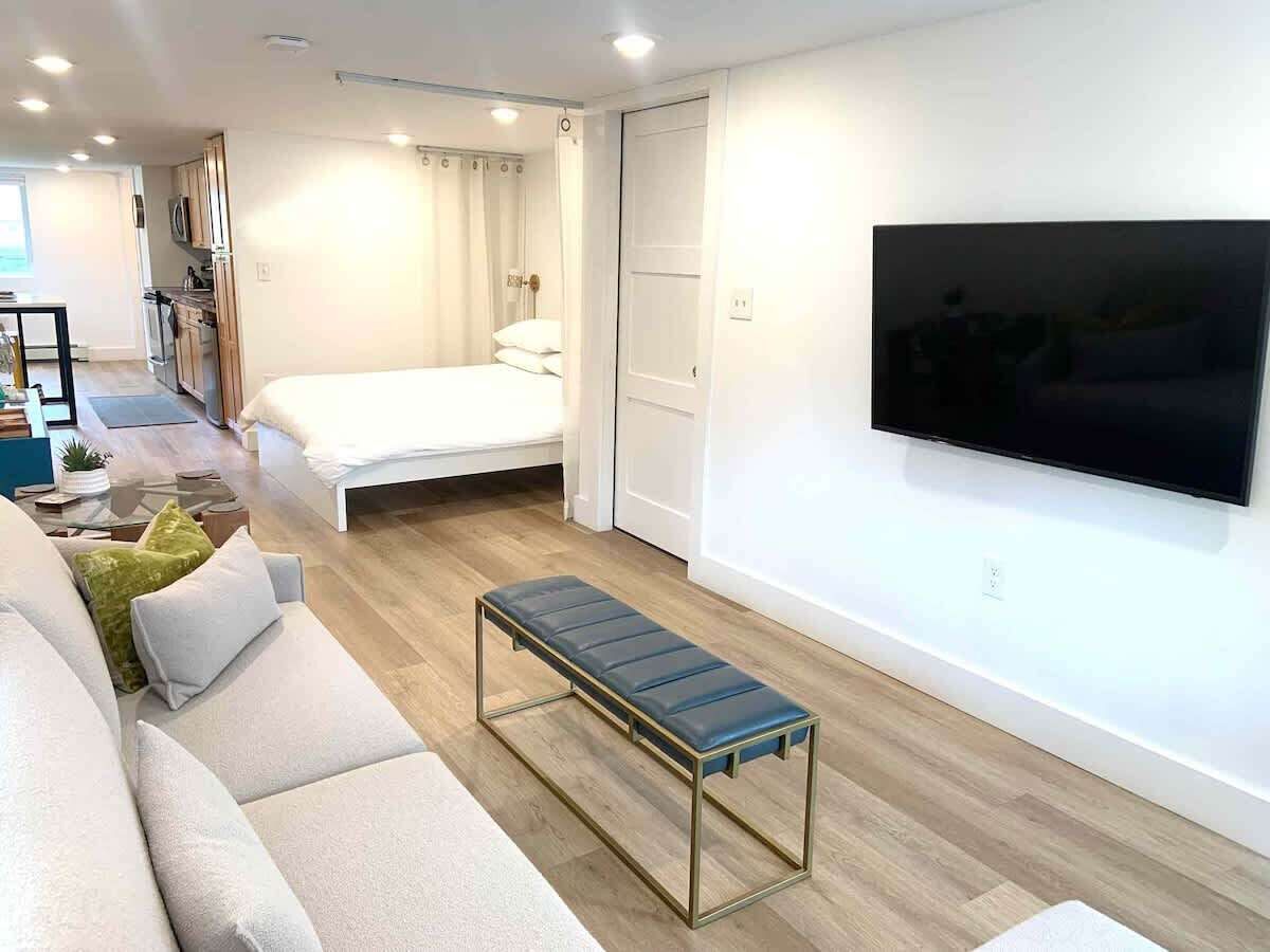 Ein modernes Wohnzimmer mit Sofa, Sitzbank, Bett, Fernseher und Küchenzeile.