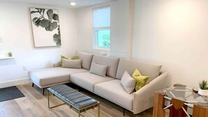 A modern living room with a sectional sofa, a glass coffee table, and a bench. - Fresh + Modern Garden Level Kittery Studio (Kittery)