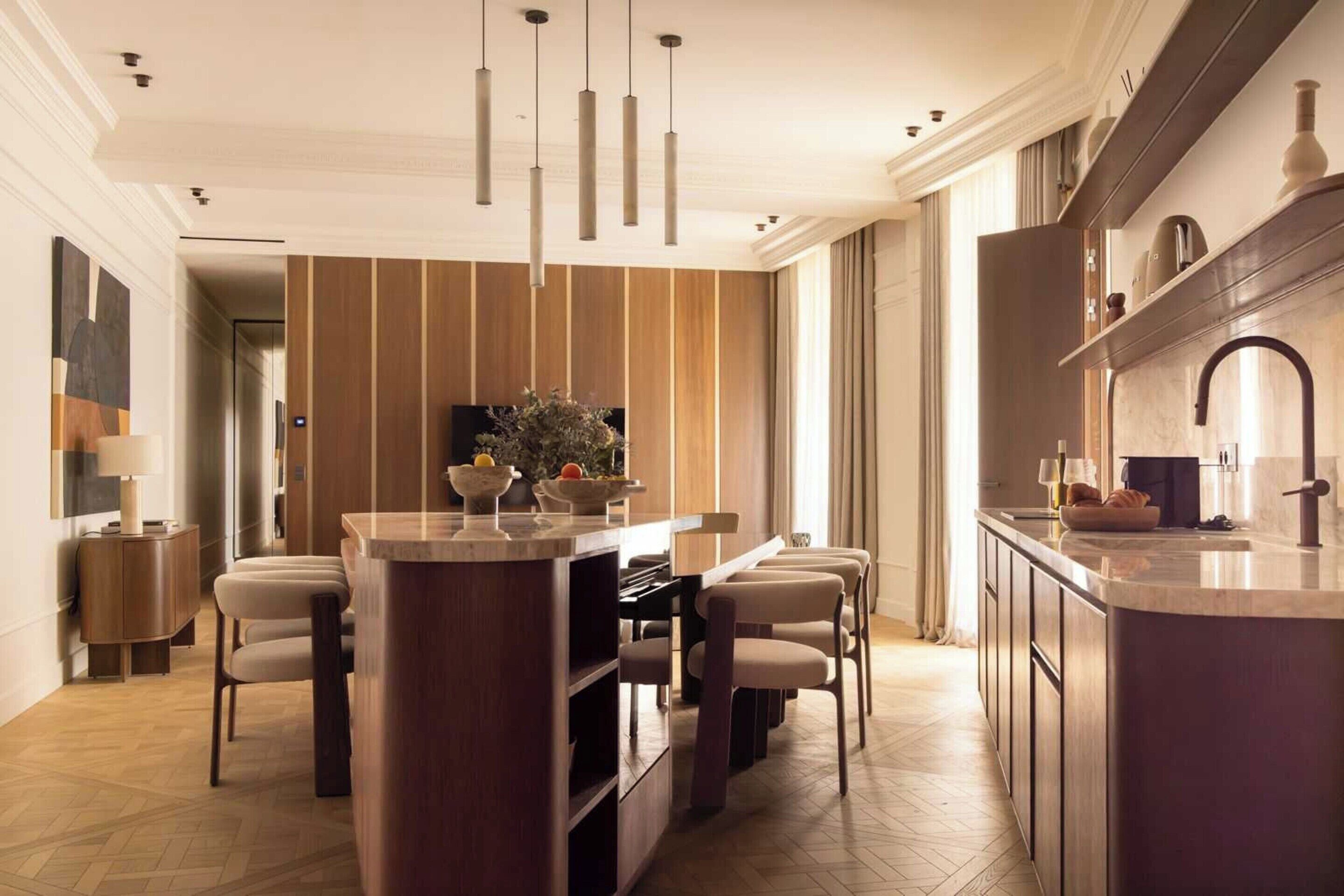 Una cocina moderna con una isla central, iluminación colgante y un comedor con sillas.