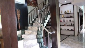 Una escalera con escalones de mármol y barandillas de metal que conduce a una habitación con una pared oscura y un jarrón decorativo.