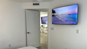 A bedroom with a bed, a TV on the wall, and a door leading to another room. - Naples Pier Condo 123 (Naples)