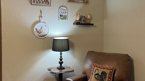 En brun læderarmstol med en dekorativ pude, et lille bord med en lampe, og vægdekorationer inklusive et skilt med 'Welcome' og et skilt med 'Farmhouse'.