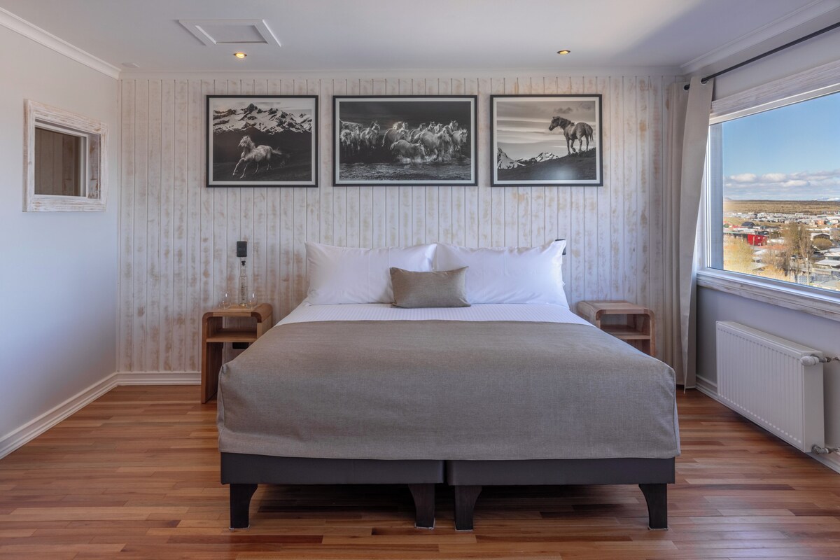 A bedroom with a large bed, a nightstand, a bedside table, and a window with a view.