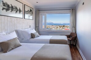 A hotel room with two beds, a view of a town and mountains, and a window with curtains. - Hotel La Tropilla (Natales)
