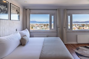 A bedroom with a bed, a view of a town, and a window with curtains. - Hotel La Tropilla (Natales)