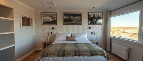 A bedroom with a large bed, wooden panel walls, framed pictures, and a window with a view.